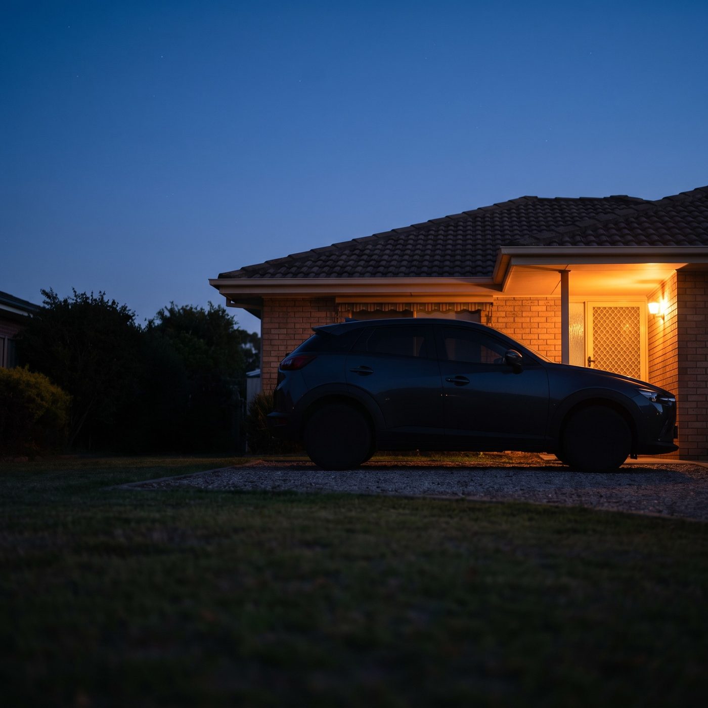 A car parked in a driveway at dusk, under a porch light