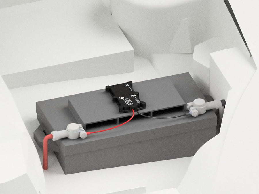 The tracker lying on top of a vehicle battery, its red and black wires on the terminals